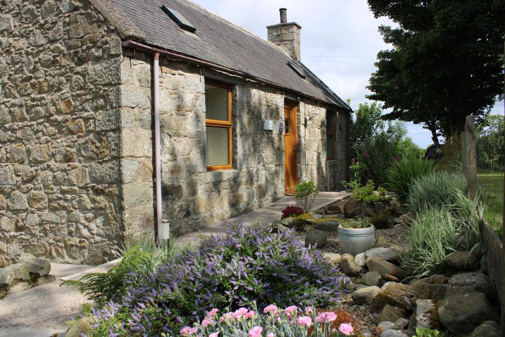 an old stone house with flowers in front of it at Buttermere Cottage in Banff