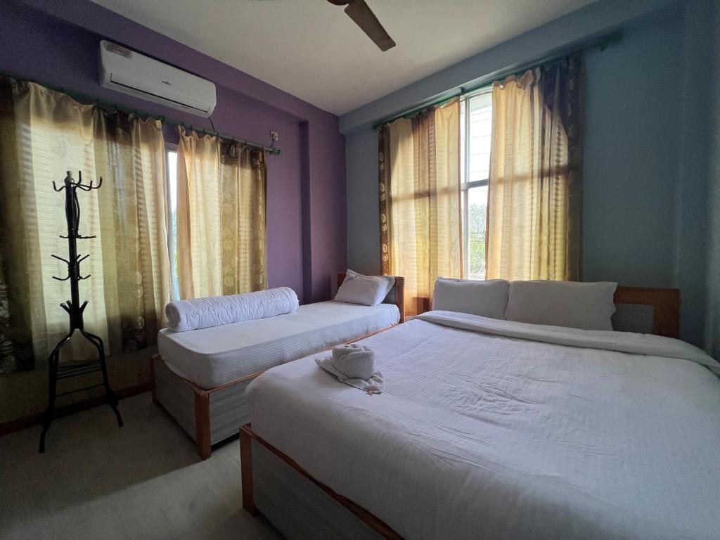 two beds in a bedroom with purple walls and windows at Three Angels Lodge & Restaurant in Chitwan