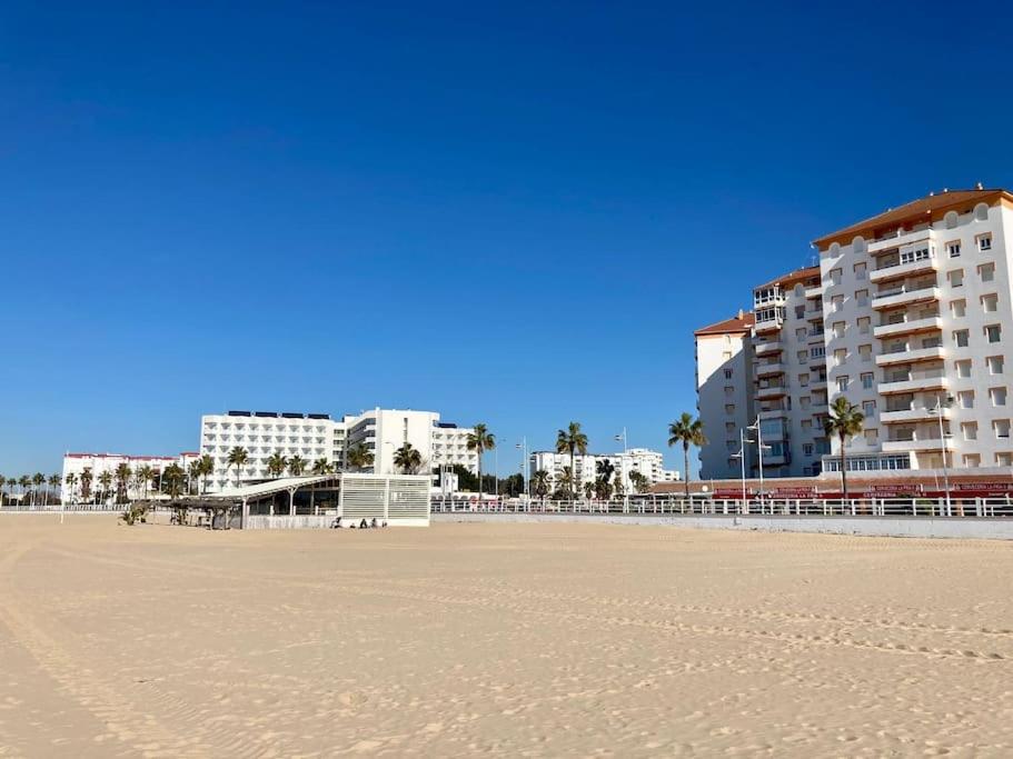 a sandy beach with buildings and palm trees and buildings at APARTAMENTO VALDEMAR PLAYA - WiFi & Aparcamiento in El Puerto de Santa María