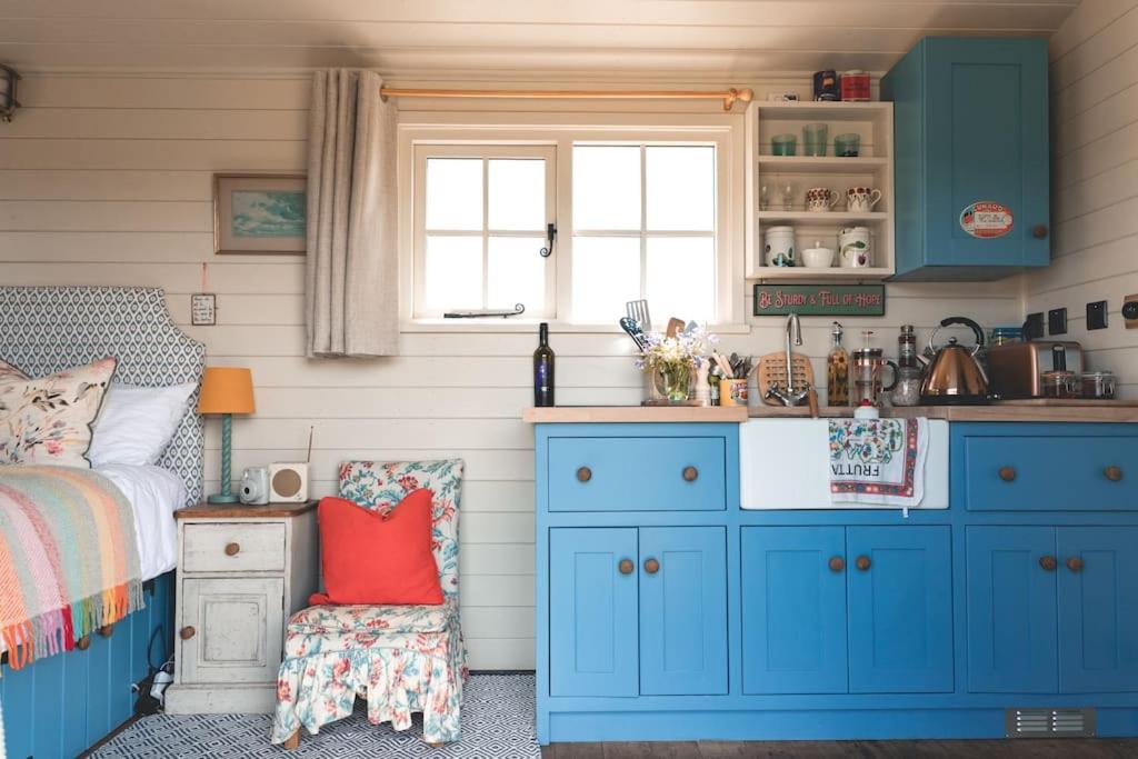 uma cozinha com armários azuis e uma cama num quarto em Dog friendly Beautifully furnished Shepherds Hut set in the Kent Countryside em Aldington