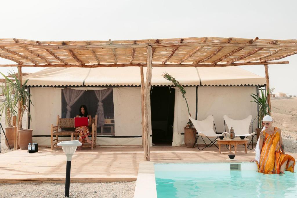 a woman sitting in a chair on a patio with a pool at Selina Agafay Nomad Camp in El Karia