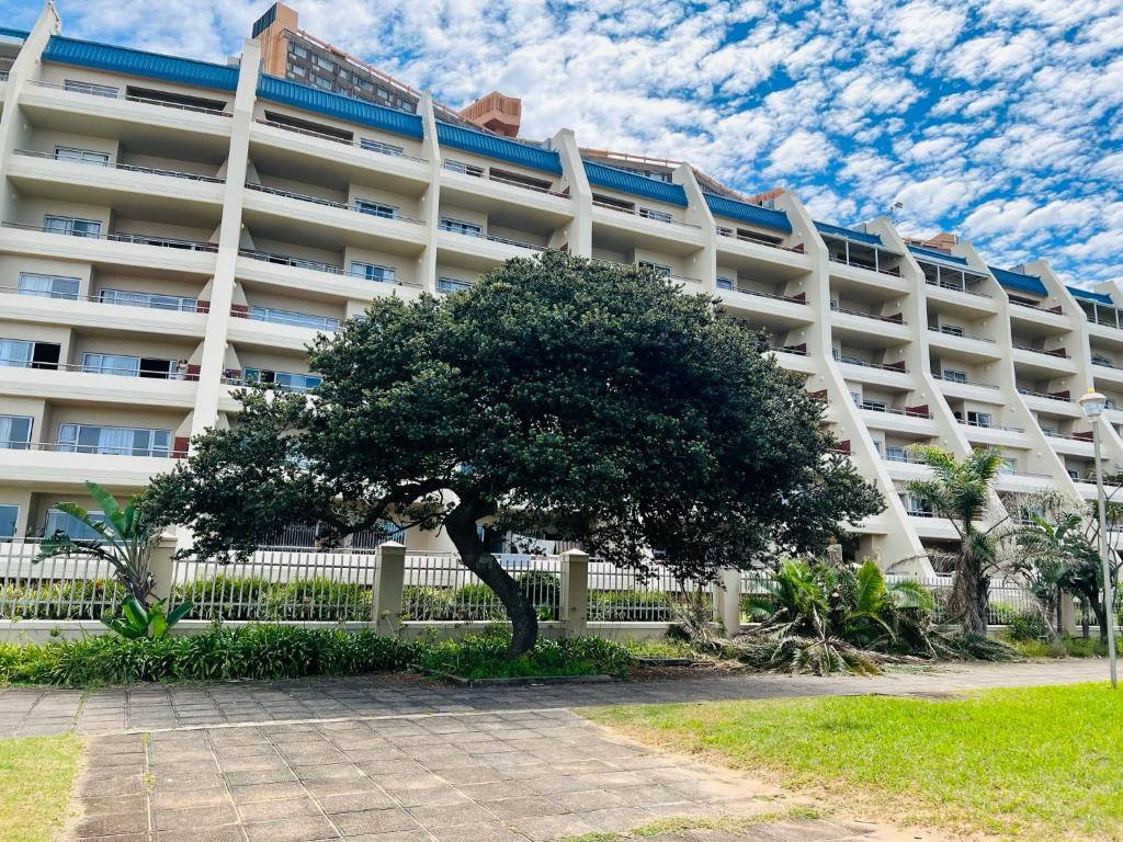 a tree in front of a large building at L’Escalier Cabanas 510 in Amanzimtoti