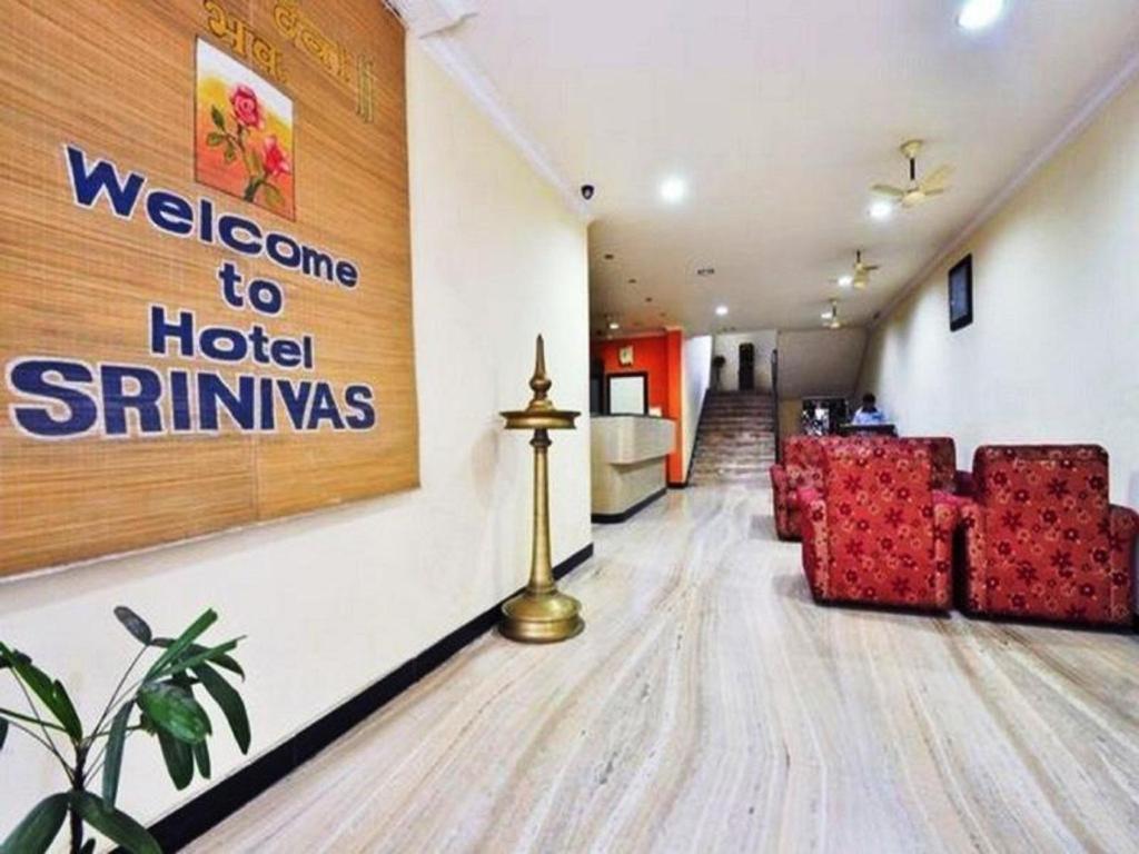 una sala de espera con sillas rojas y una señal de bienvenida al hotel siminus en Hotel Srinivas, en Kochi