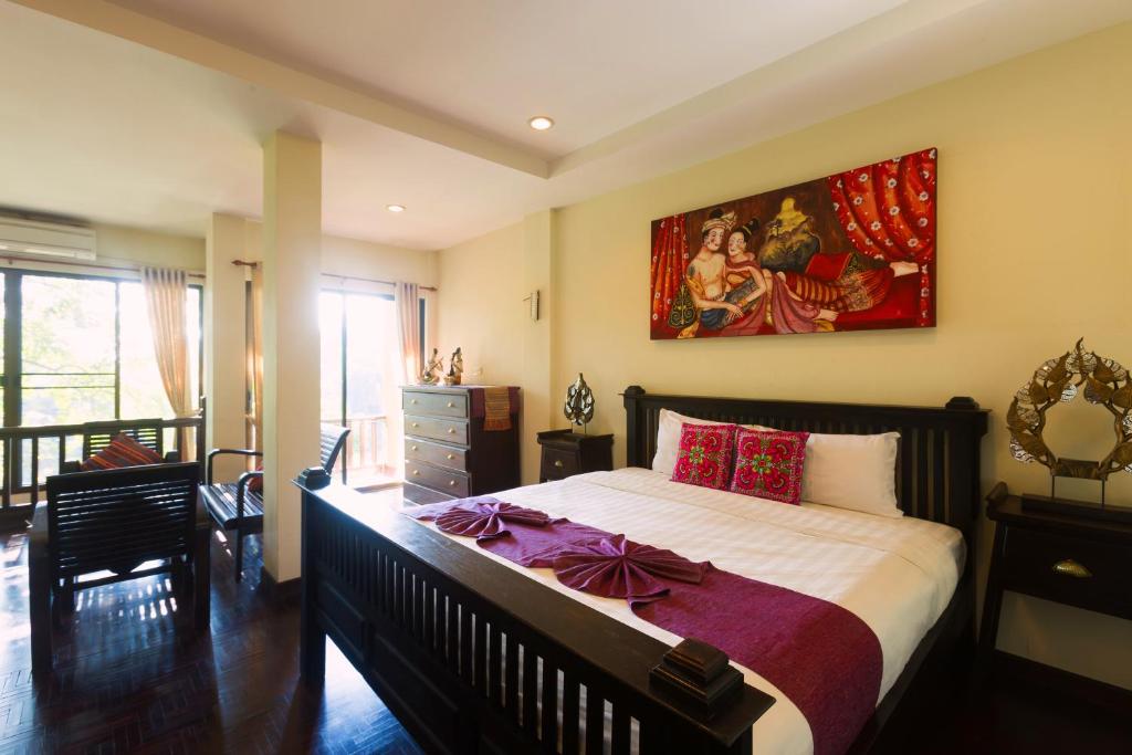 A bright bedroom with a dark wooden four-poster-style bed and a sitting area beside tall windows.
