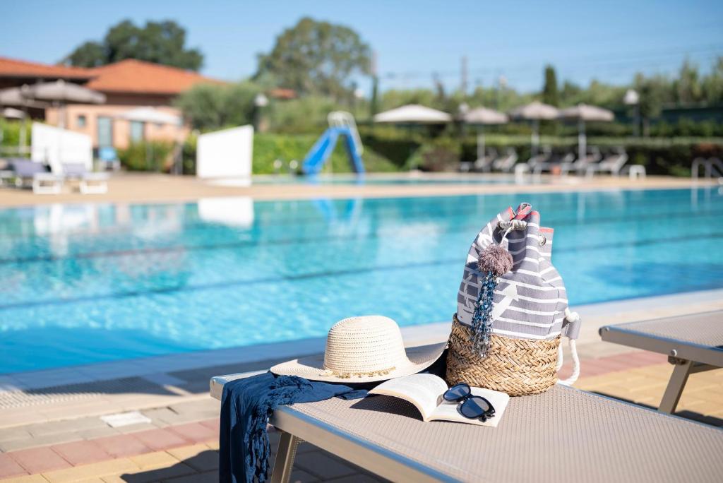 un sombrero y un libro sentado en un banco junto a una piscina en Villaggio Il Girasole, en Follonica
