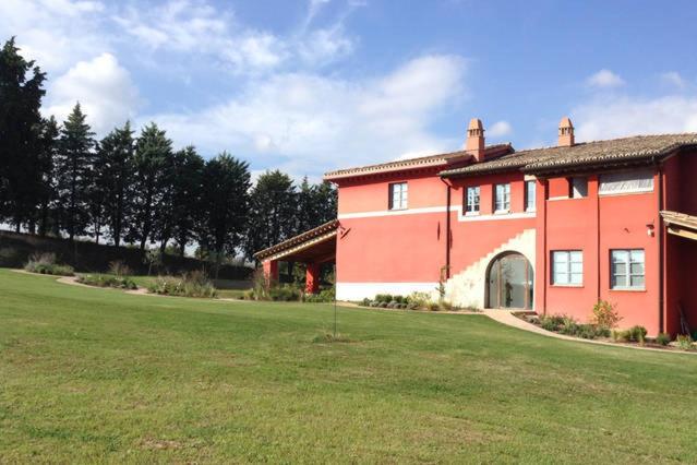 a large red house with a large grass field at Al Dolce Far Niente Dimora con piscina di Design in San Biagio della Valle