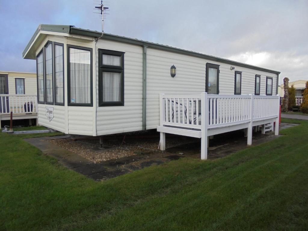 a white tiny house with a porch on a lawn at 8 Berth Central heated Golden Palm (Aspen GP) in Chapel Saint Leonards