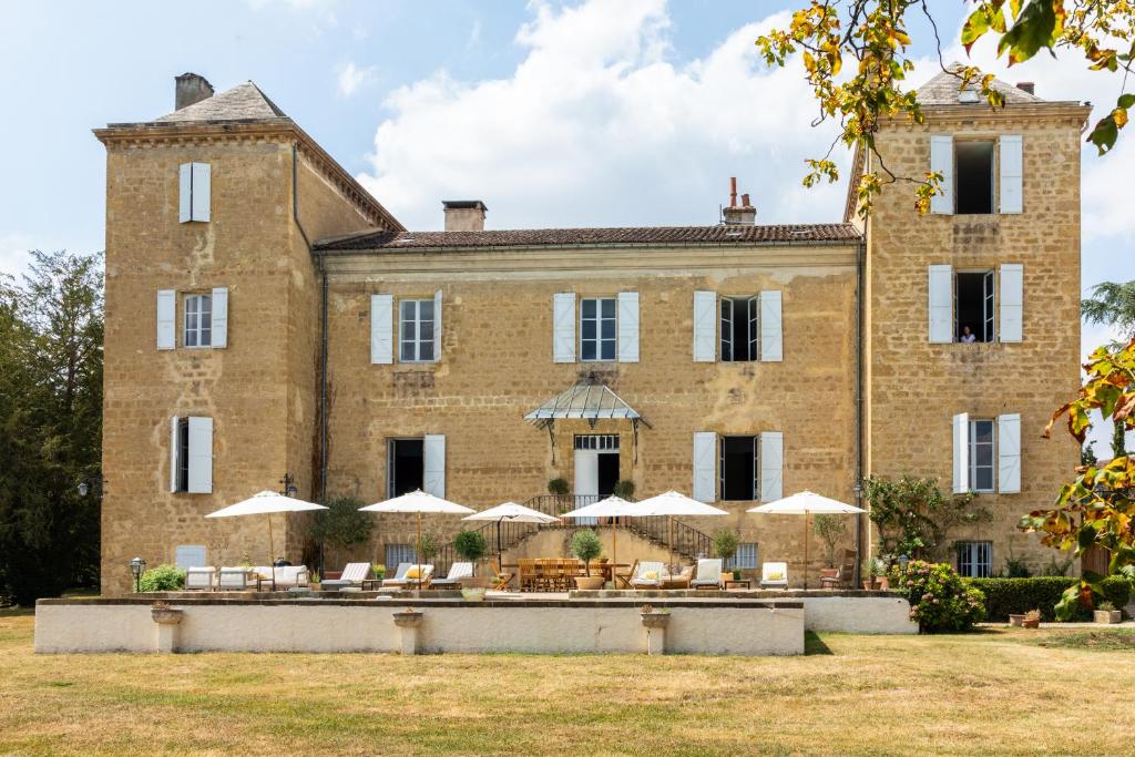 Ornézan的住宿－Stunning refurbished Chateau in South West France，一座带桌子和遮阳伞的大型砖砌建筑