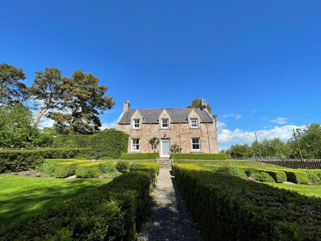 uma antiga casa de tijolos com um caminho para um jardim em Balloan Cottage em Dornoch