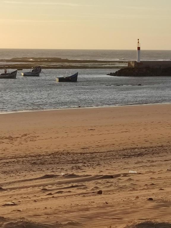 una playa con barcos en el agua y un faro en villa swiriya atlantique, en Souira Guedima