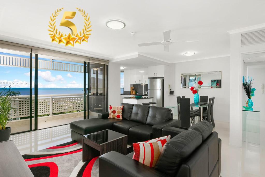 a living room with a black couch and a kitchen at Cairns Luxury Waterfront Apartment in Cairns
