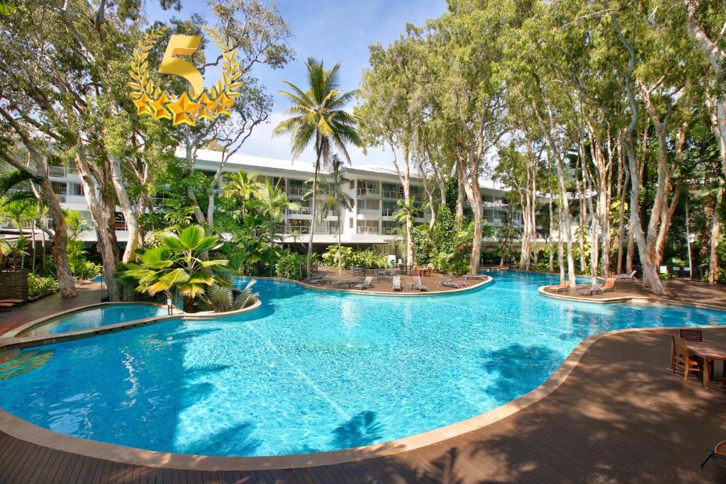 a large pool with trees in front of a building at Palm Cove Beach Apartment in Palm Cove