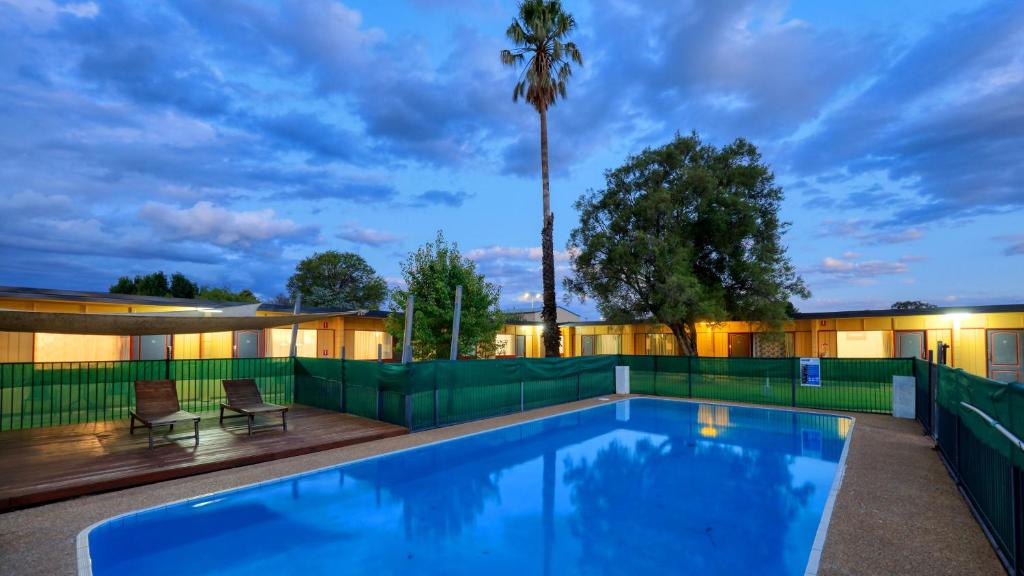 a swimming pool with a fence and a palm tree at Cootamundra Gardens Motel in Cootamundra