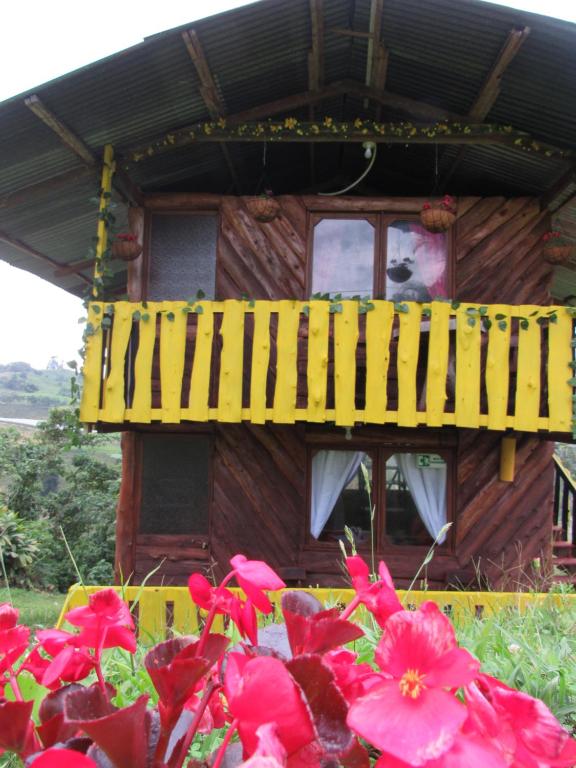 a wooden house with a yellow balcony and pink flowers at glamping/cabañas Monaco in Santa Rosa de Cabal