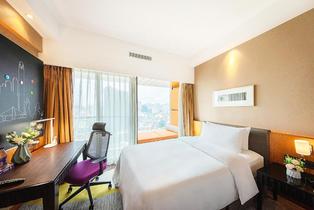 珠海市にあるHampton by Hilton Zhuhai Gongbei Portのベッド、デスク、窓が備わるホテルルームです。