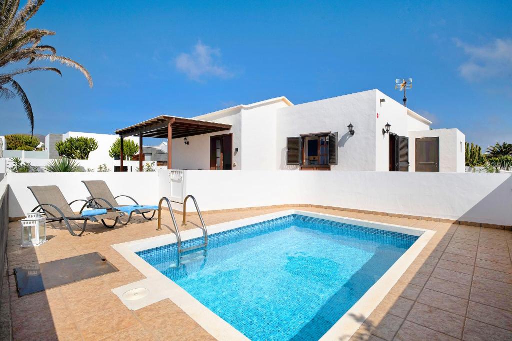 a villa with a swimming pool in front of a house at El Charco Azul in Charco del Palo