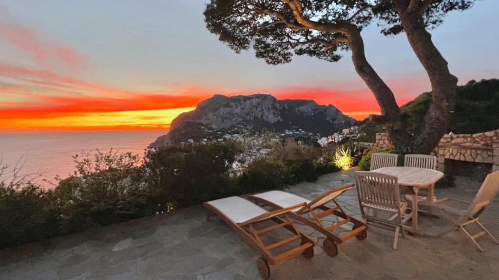 a couple of chairs and a table with a sunset at La Casetta delle Api in Capri
