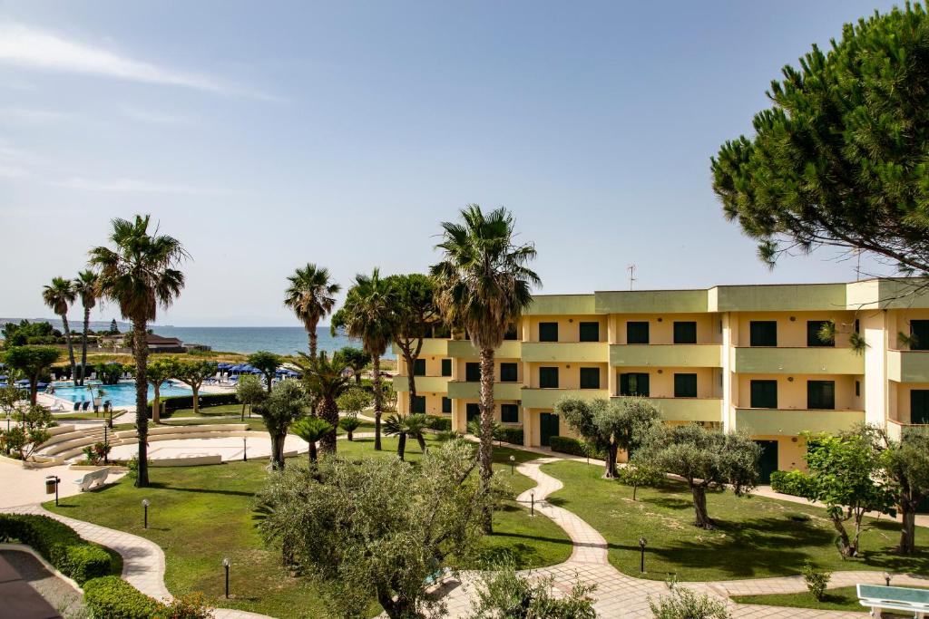 a view of a building with palm trees and the ocean at Hotel Village Paradise in Mandatoriccio Marina