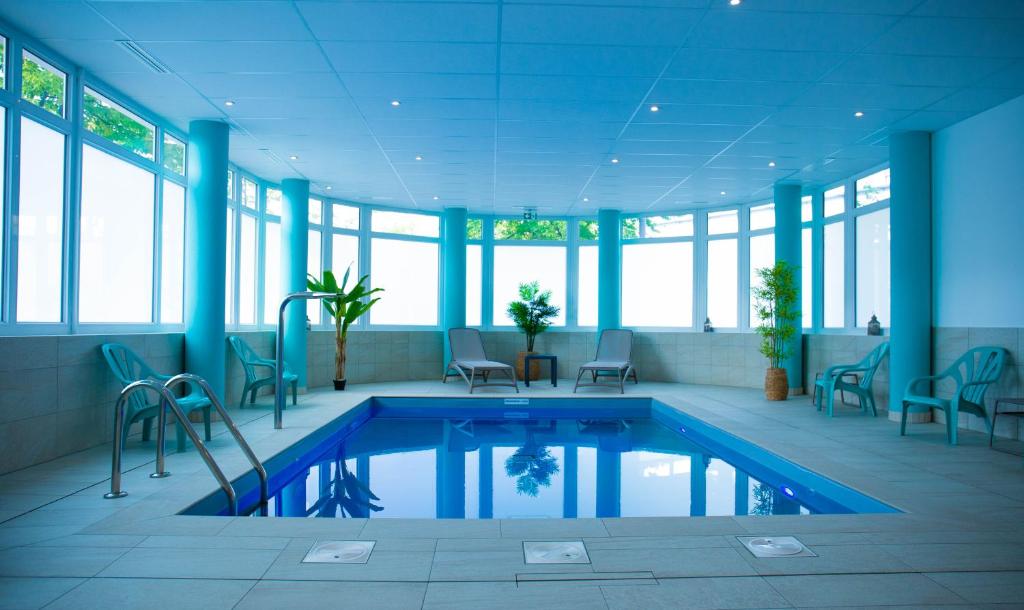 einen Pool in einem Gebäude mit Stühlen und Fenstern in der Unterkunft Lagrange Apart Hôtel Mulhouse Saint Sauveur in Mulhouse