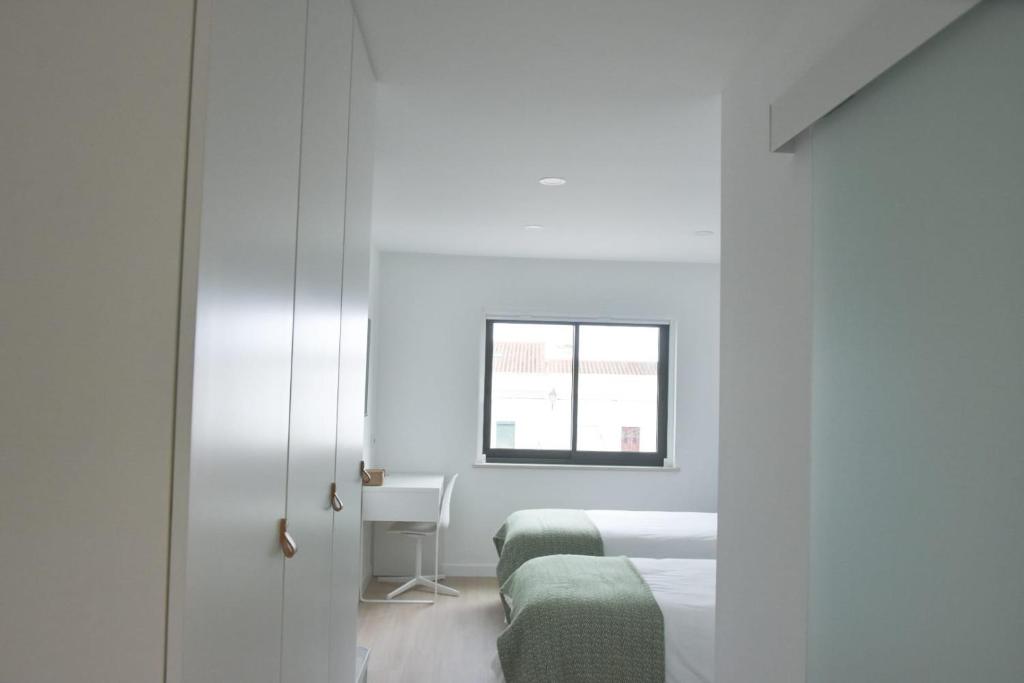 a white bedroom with two beds and a window at Sal Praça in Castro Verde