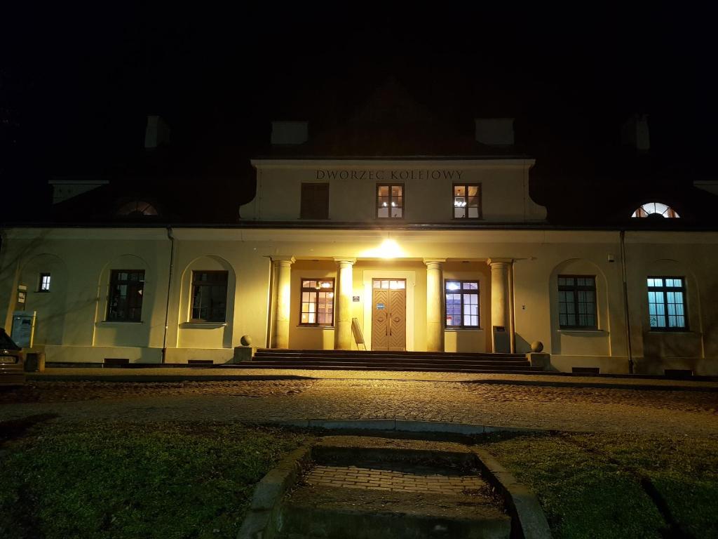 a white building with a light at night at Quadrans Hostel and Caffee na dworcu kolejowym Modlin 7 min jazdy lotniskowym autobusem wahadłowym in Nowy Dwór Mazowiecki