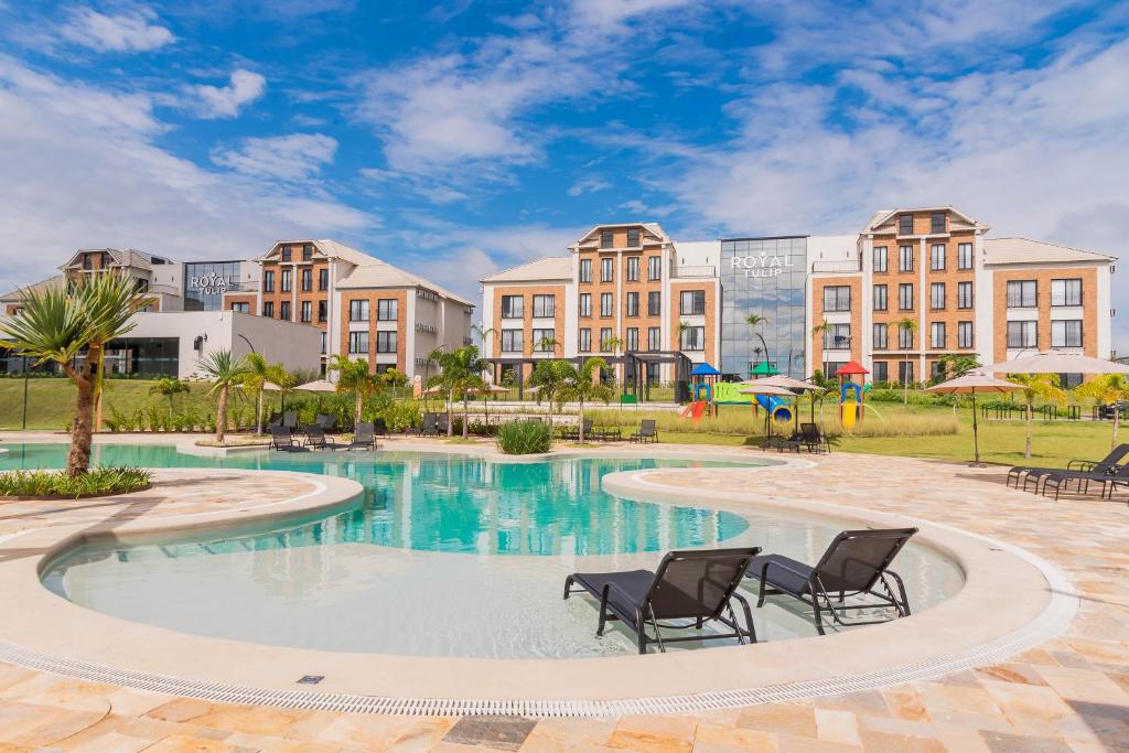 a pool with chairs and buildings in the background at Royal Tulip Holambra in Holambra