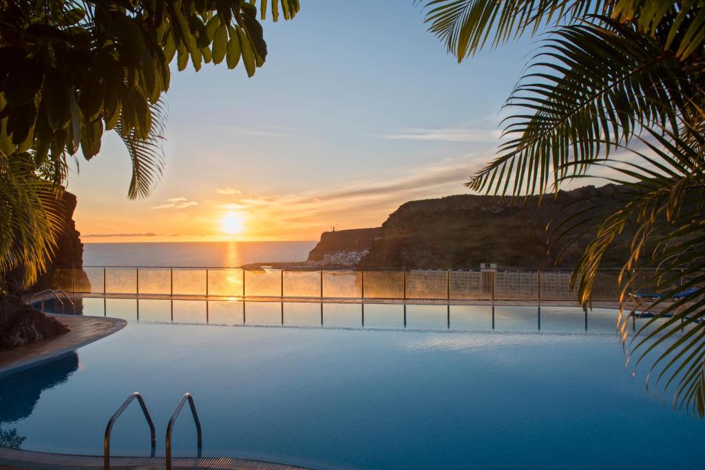 a pool with a view of the ocean at sunset at Mogan Princess & Beach Club in Taurito