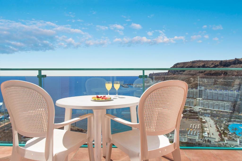 a table with two chairs and wine glasses on a balcony at Mogan Princess & Beach Club in Taurito