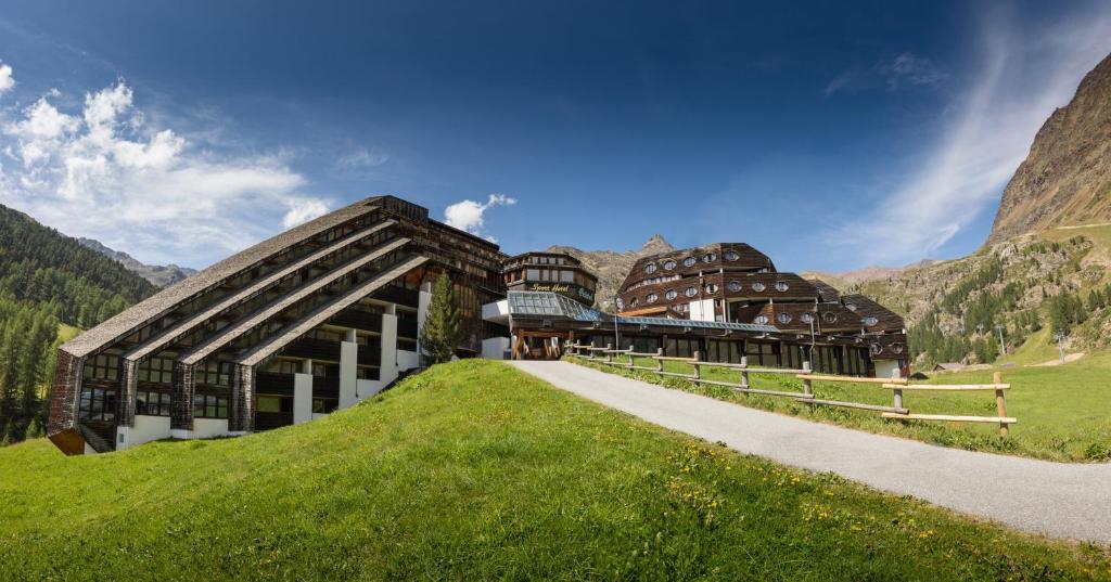 un edificio su una collina erbosa con una montagna di Blu Hotel Senales Zirm-Cristal a Maso Corto