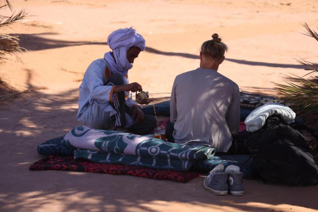 two people sitting on a blanket on the ground at Bivouac Beauté de Désert in Mhamid