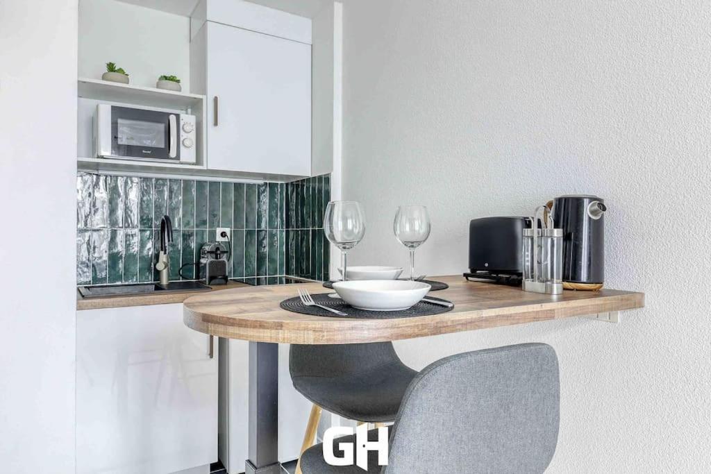 - une cuisine avec une table, un four micro-ondes et des verres à vin dans l'établissement Le P’tit Bussy - Magnifique studio proche Disneyland & Paris, à Bussy-Saint-Georges
