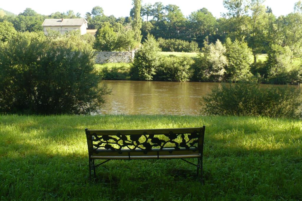 a park bench sitting in the grass next to a river at Les Délices de Lavoûte in Lavoûte-sur-Loire