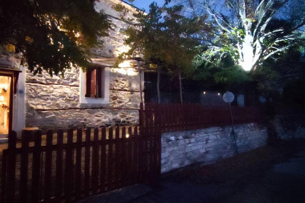 a house with a fence in front of it at night at COZY VILLAGE HOUSE ΑΓΙΟΣ ΛΑΥΡΕΝΤΙΟΣ ΠΗΛΙΟΥ in Agios Lavrentios