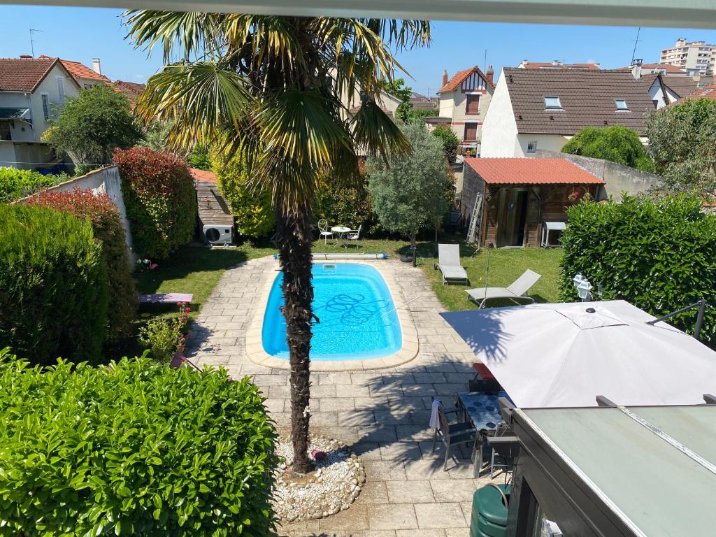 uma palmeira ao lado de uma piscina com um guarda-sol em Laetisteph em Neuilly-sur-Marne