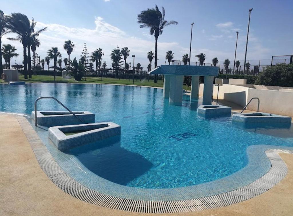 una gran piscina de agua azul con palmeras en Marina Serena Golf 1ª linea Playa, en Roquetas de Mar