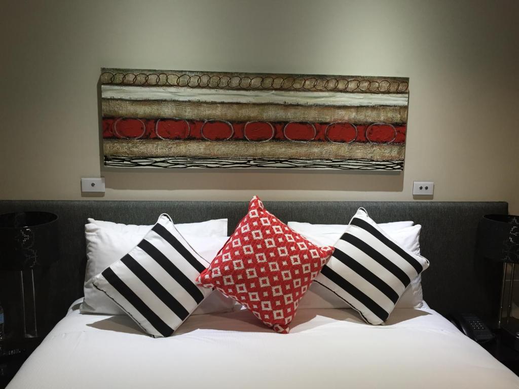 a bed with pillows on it with a painting on the wall at Calamvale Hotel Suites and Conference Centre in Brisbane