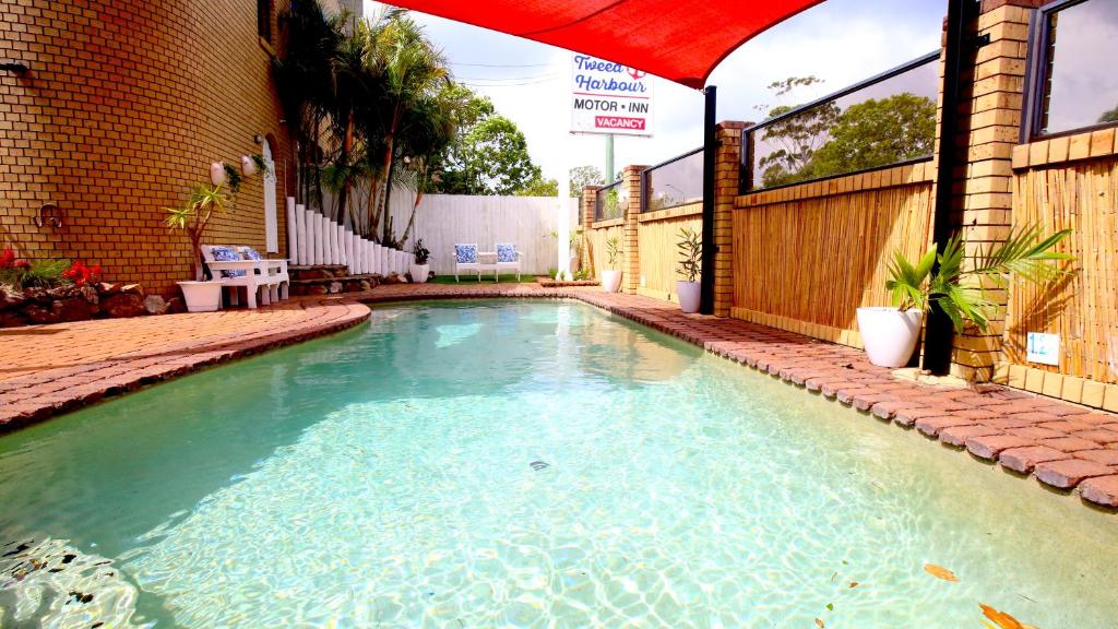 a swimming pool with blue water and a red umbrella at Tweed Harbour Motor Inn in Tweed Heads