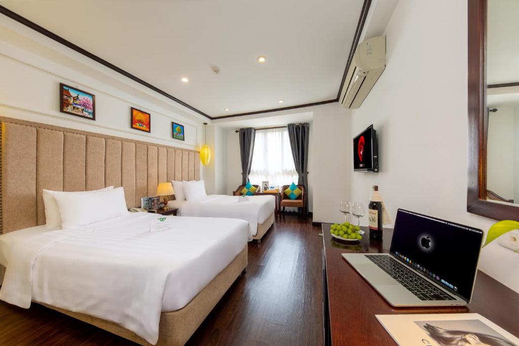 a hotel room with two beds and a desk with a laptop at Babylon Grand Hotel & Spa in Hanoi