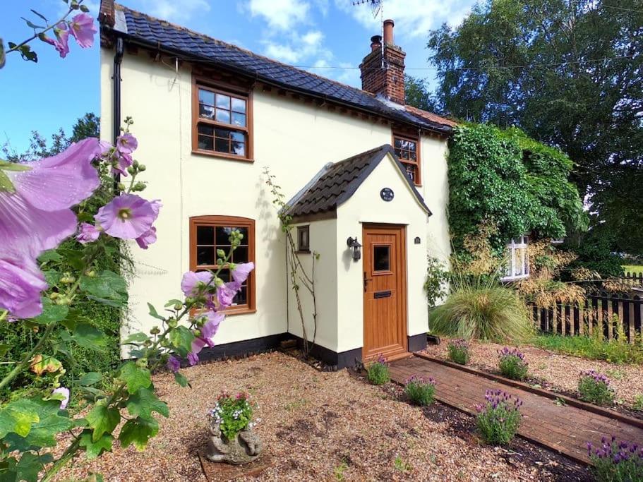 ein kleines weißes Haus mit einer Tür und Blumen in der Unterkunft Rose Cottage, 2 Bedroom Cottage with character, near Southwold in Wrentham