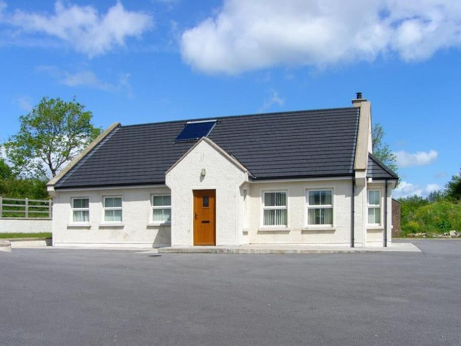 biały budynek z czarnym dachem i pomarańczowymi drzwiami w obiekcie Fermanagh Holiday Home w mieście Newtown Butler