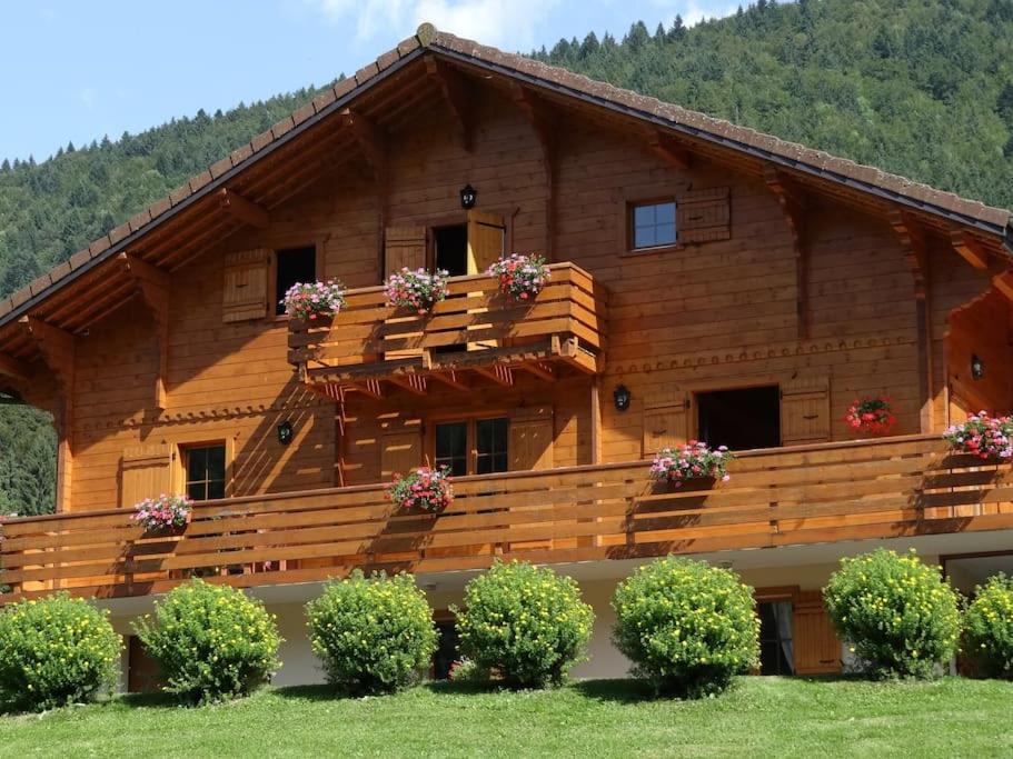 a large wooden house with flowers on the balcony at Lélex, appartement "HERMINE" dans chalet, piscine couverte in Lélex