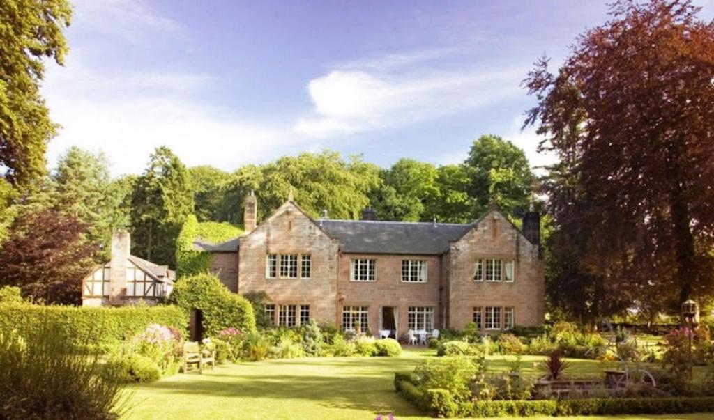 a large brick house with a garden in the yard at Trigony House Hotel and Garden Spa in Closeburn