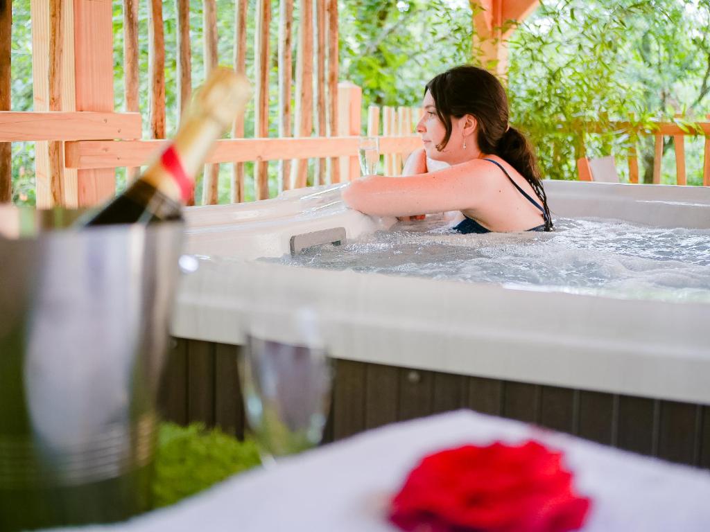 une femme dans un bain à remous avec une bouteille de vin dans l'établissement Cabane Château hôtel luxe avec spa privatif Aulteribe - Le Peydébé, à Vieille-Brioude