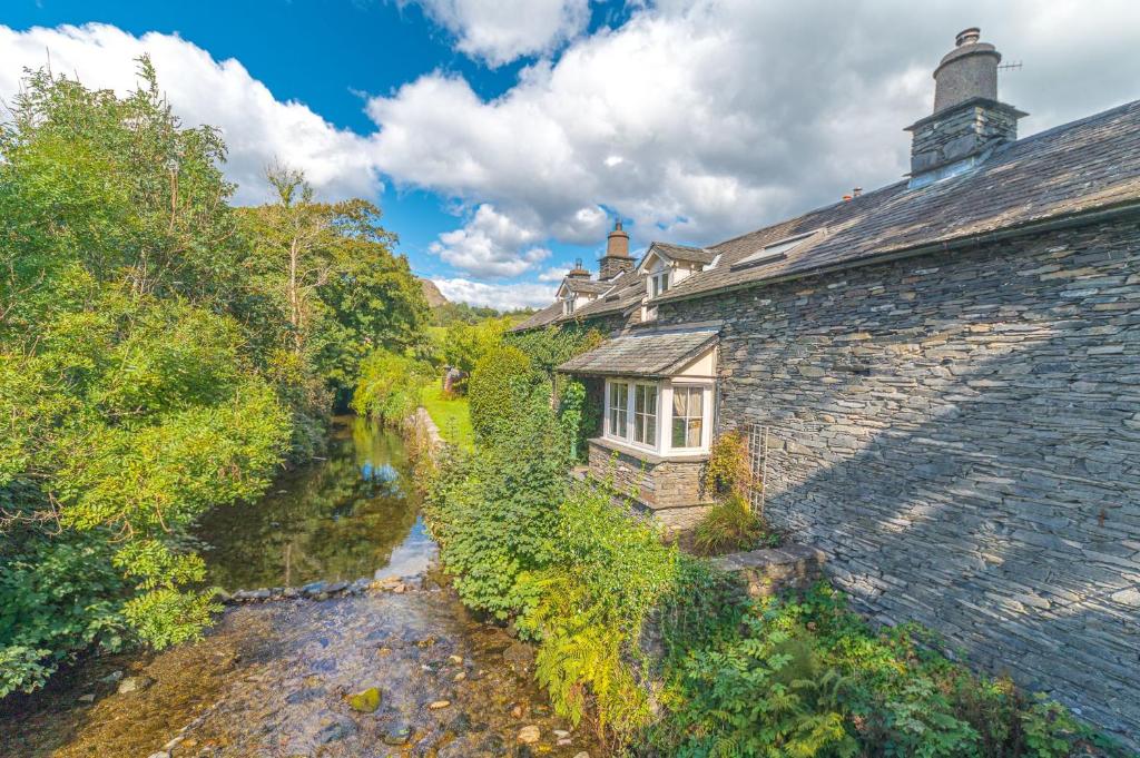 an old stone building with a window next to a river at Smithy Cottage Coniston in Coniston