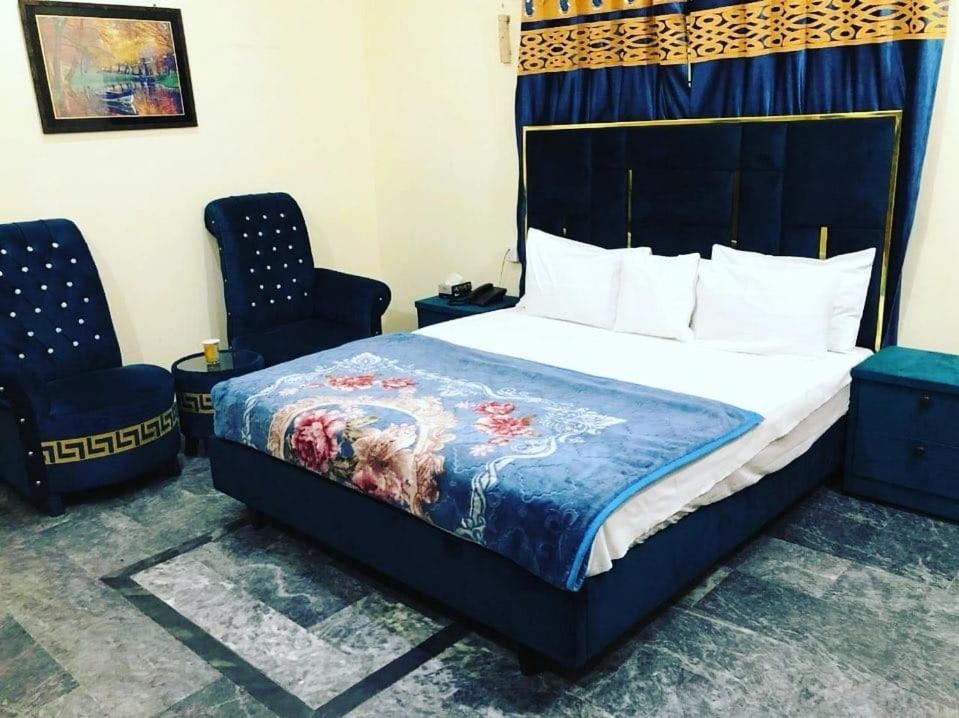 a bedroom with a bed with a blue bedspread and two chairs at Hotel Air inn in Lahore