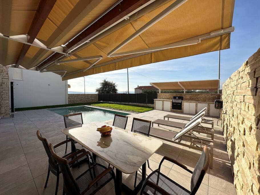 eine Terrasse mit einem Tisch, Stühlen und einem Pool in der Unterkunft Holiday house NiRi with a heated outdoor pool /BBQ in Kaštela