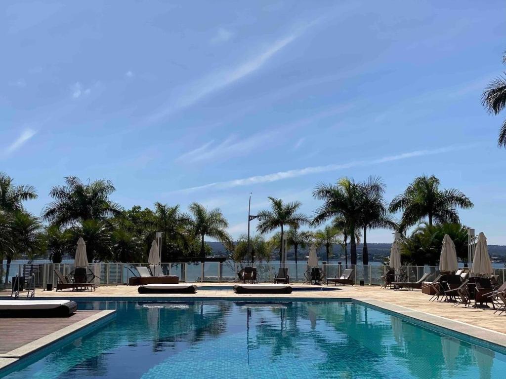 uma piscina com cadeiras e guarda-sóis e palmeiras em Harmonia à Beira do Lago - Life Resort em Brasília