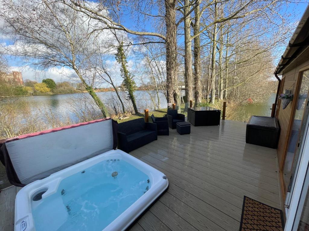 une baignoire jacuzzi sur une terrasse à côté d'un lac dans l'établissement Rudd lake Luxury lakeside lodge with fishing & hot tub@Tattershall, à Tattershall