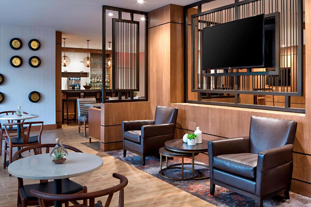 a waiting room with tables and chairs and a flat screen tv at Houston Marriott Westchase in Houston