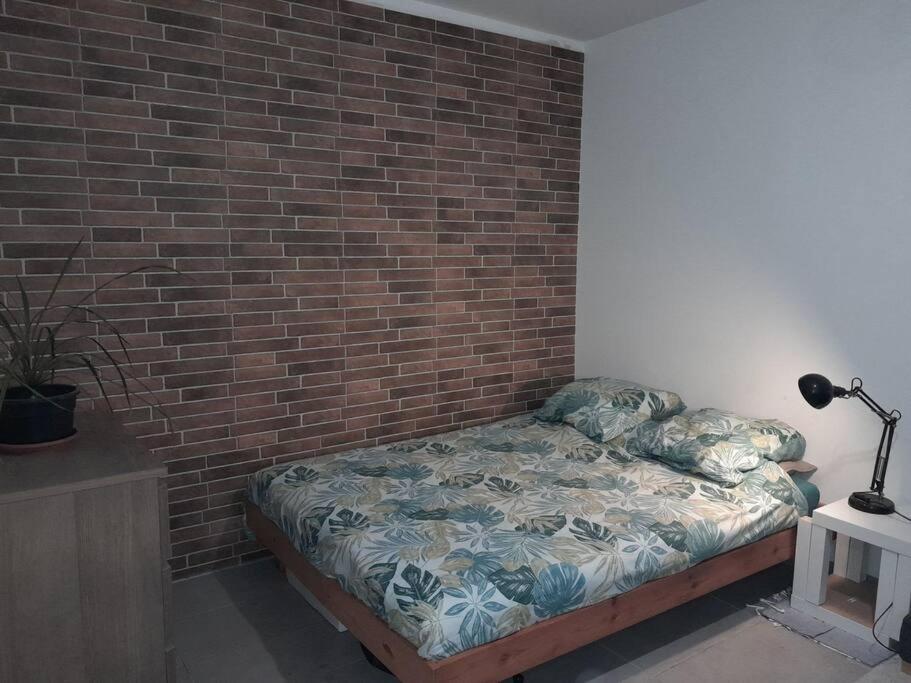 Un dormitorio con una pared de ladrillo y una cama en Studio agréable et fonctionnel à 5km des plages, en Lannion